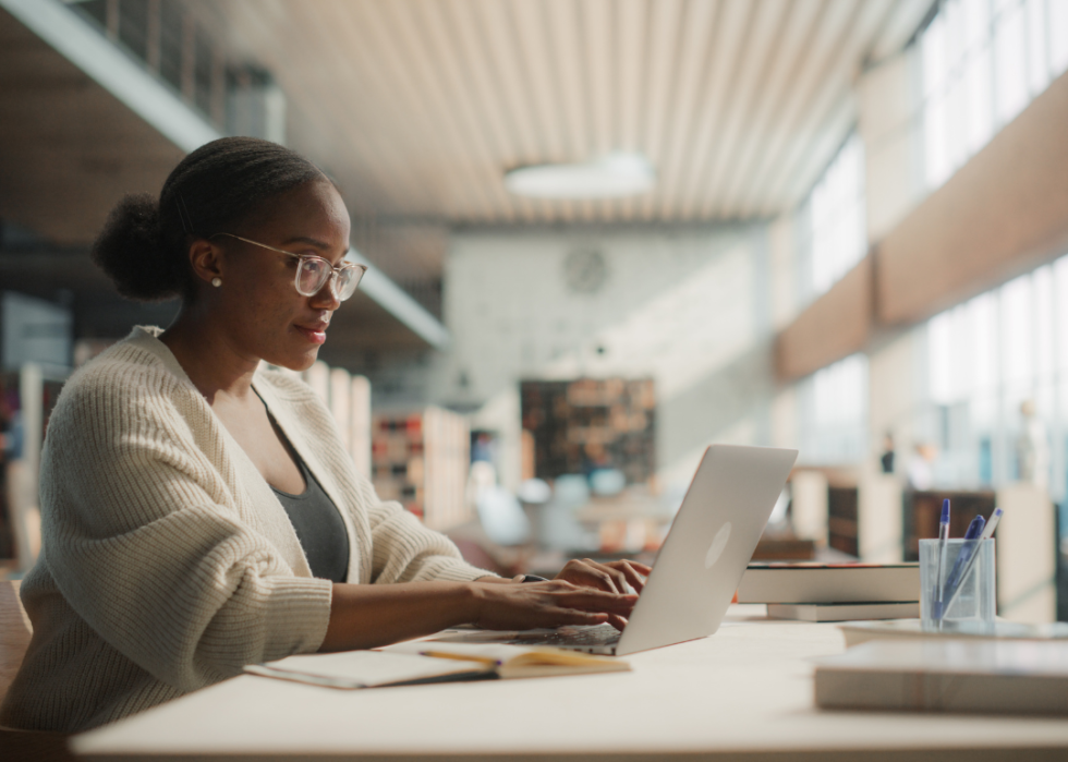 A young woman working on a laptop in a library.