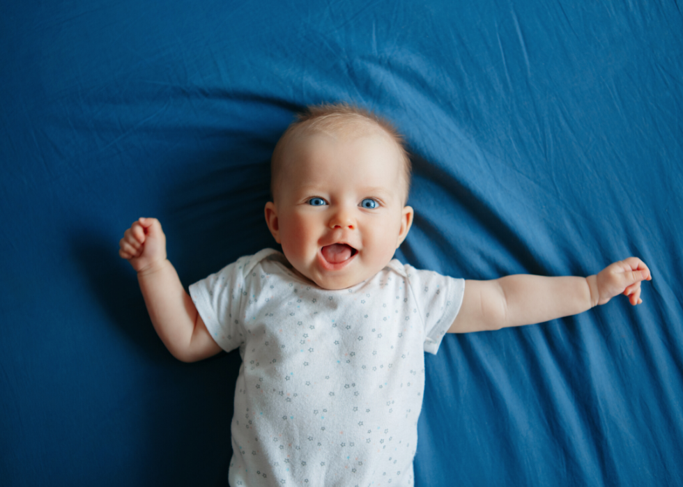 Smiling baby with blue eyes lying on bed looking at camera.