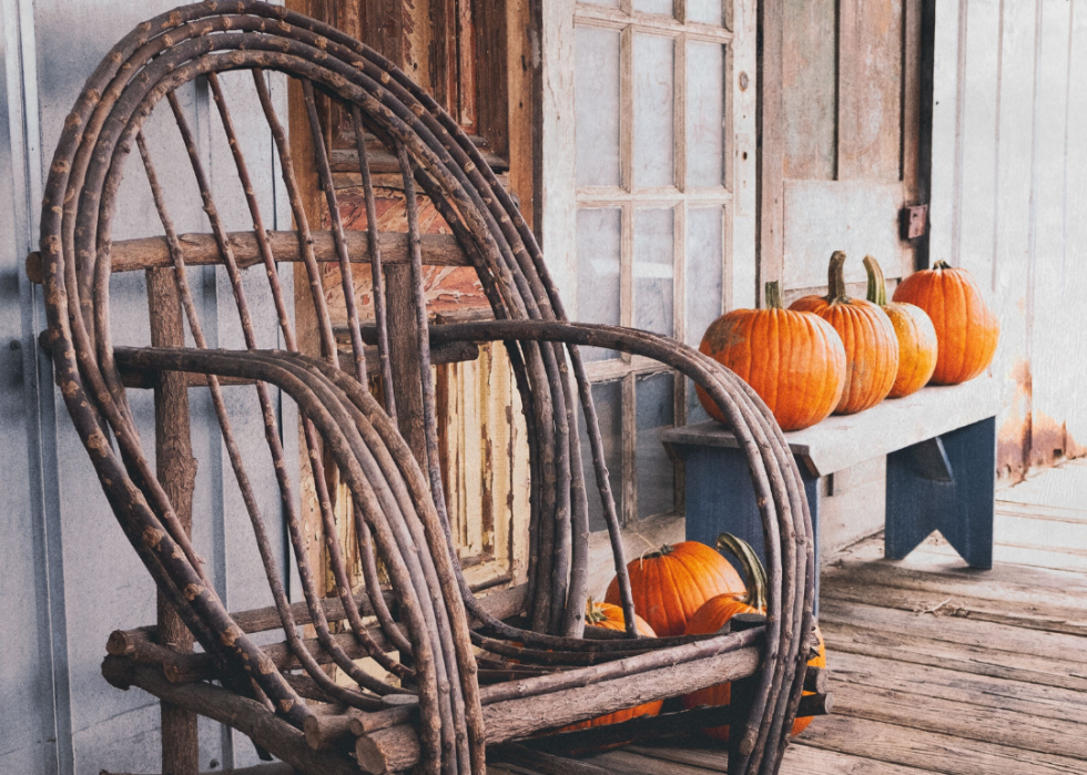 A rustic wooden rocking chair and pumpkins on a porch.