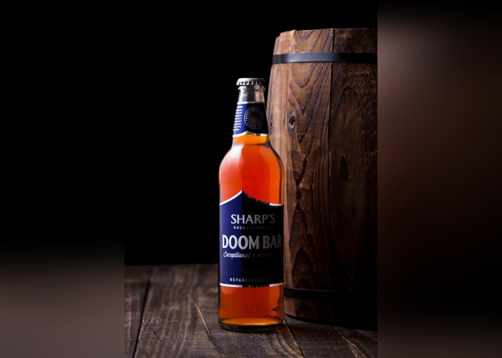 Bottle of Sharp's Doom Bar amber ale on with wooden barrel on a dark background.