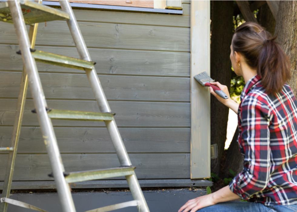 A woman painting the exterior wall of a wooden house