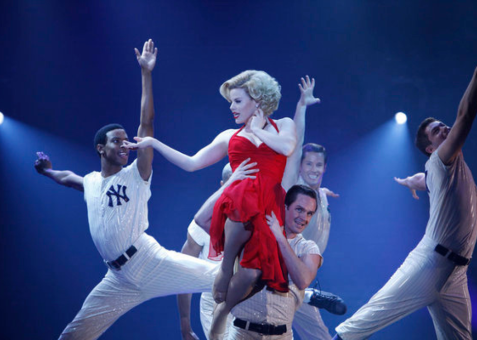Megan Hilty dancing on stage in a red dress with guys in baseball uniforms.