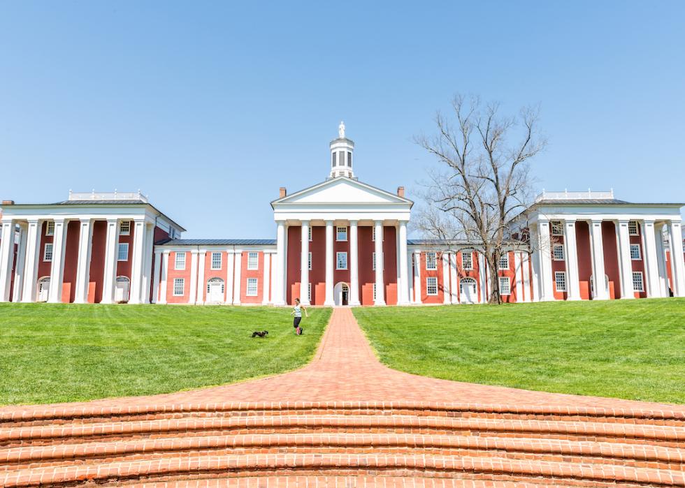 A brick pathway leads to a red building with many windows and white columns on the Washington and Lee University campus. 
