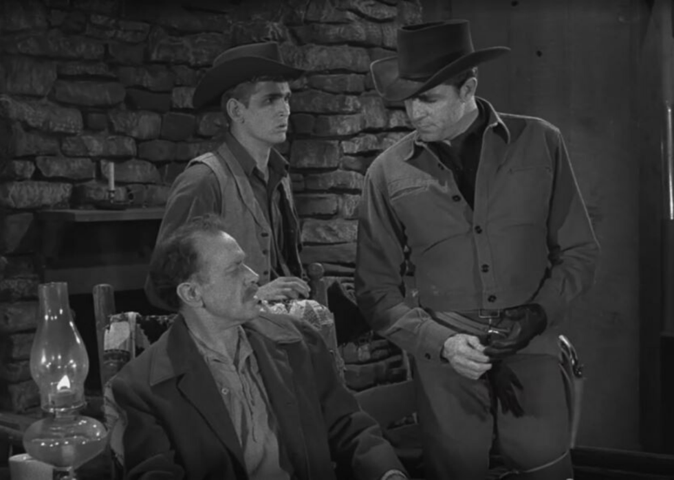 Three cowboys talking inside a house.