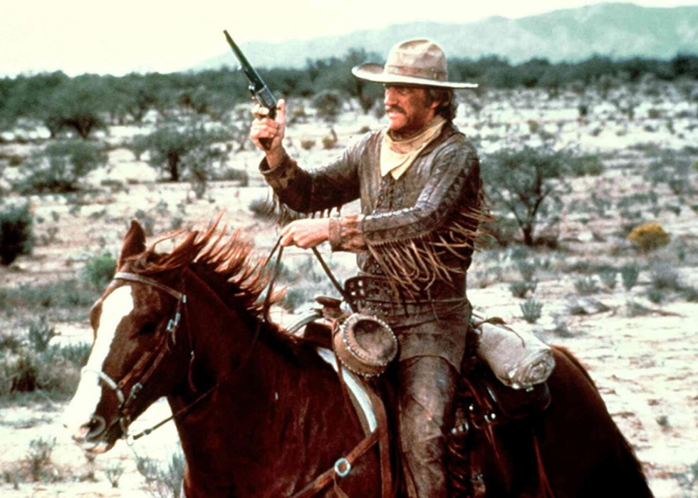 A man holding a pistol up on a galloping horse.