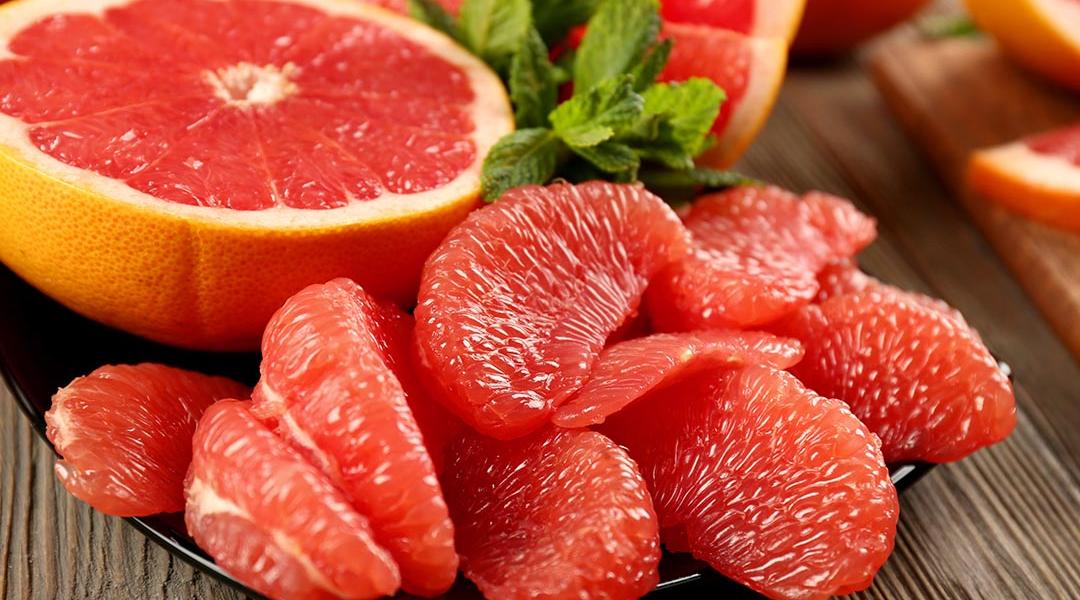 Beauty photo of sliced half a grapefruit on a black plate with peeled pieces of grapefruit in the foreground.