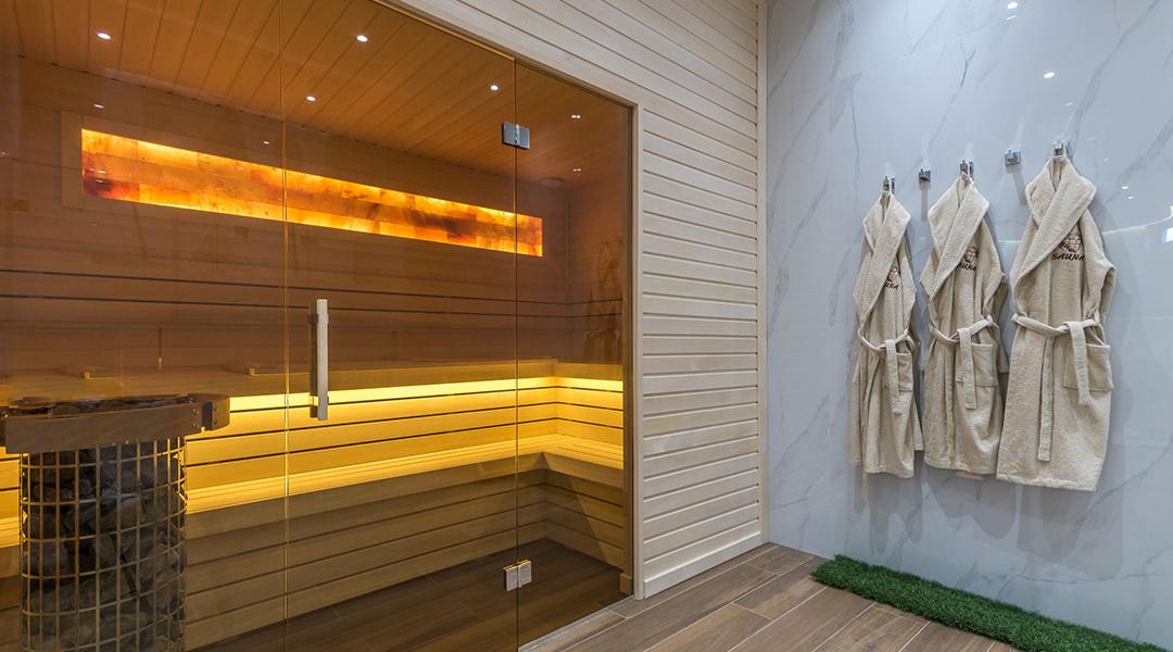 A modern home sauna with bathrobes hanging on its wall.