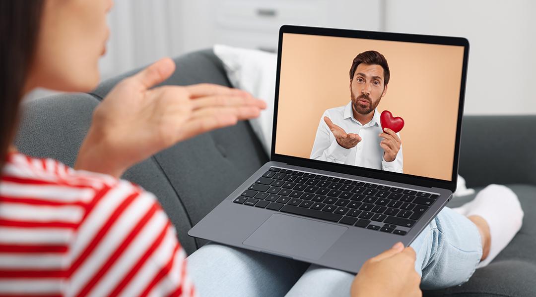 A woman blows a kiss to her partner in a video call with him using a laptop.