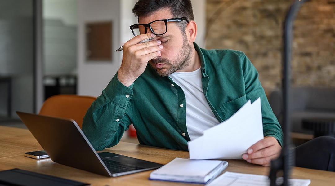 Anxious landlord rubbing eyes while looking at documents.