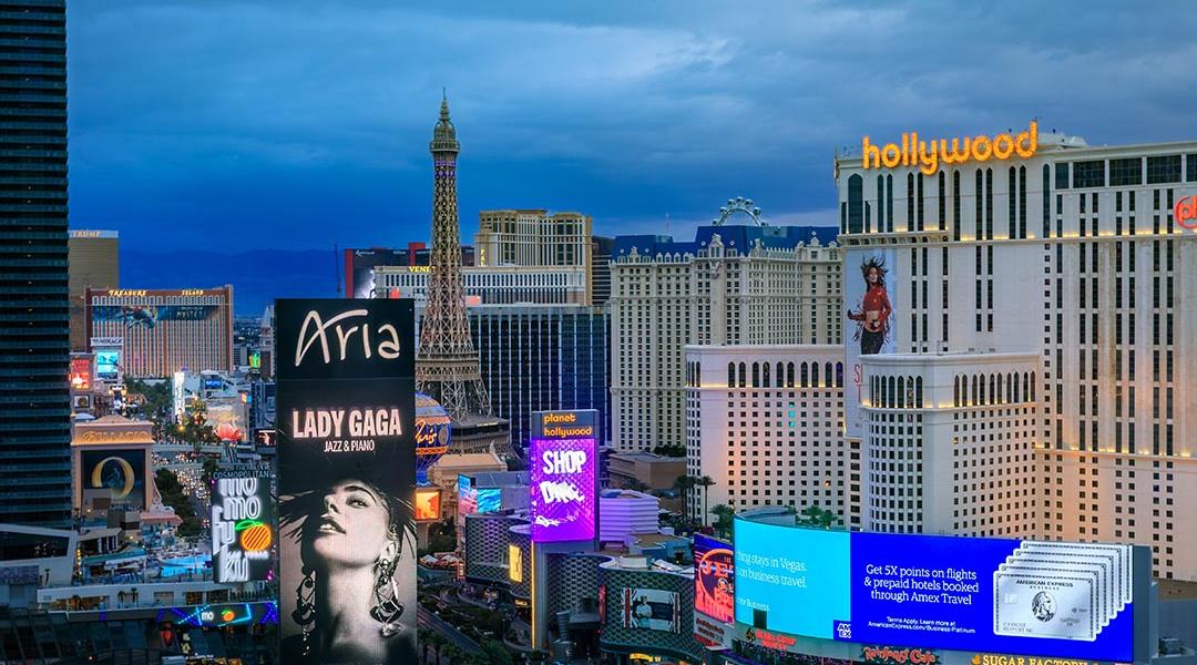 The Strip skyline in Las Vegas with advertising billboards including Lady Gaga, neon lights on iconic hotels and casinos after sunset.