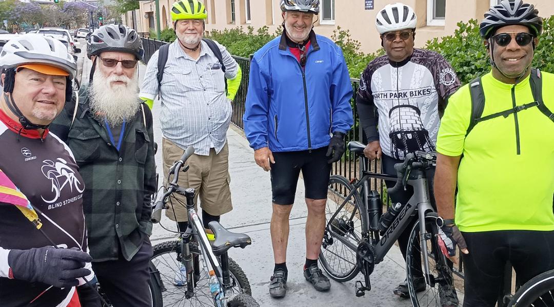 A group of participants in full biking gear posing for a photograph with their bicycles.