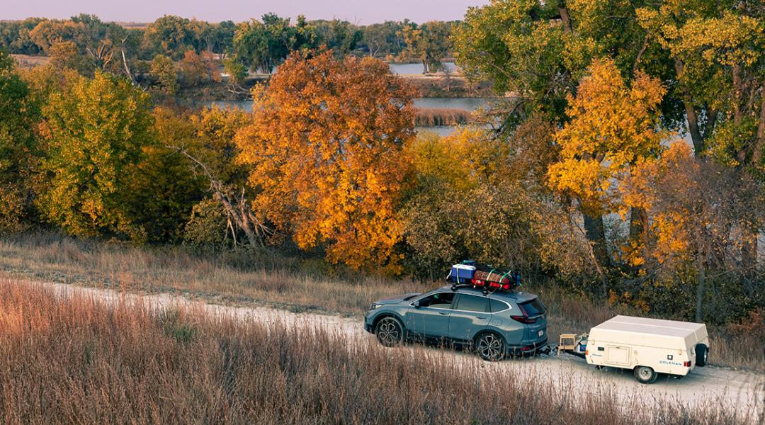 A blue 2020 Honda CR-V towing a 1990 Coleman Columbia pop-up camper on the road towards Antelope Lake in Kansas during autumn.