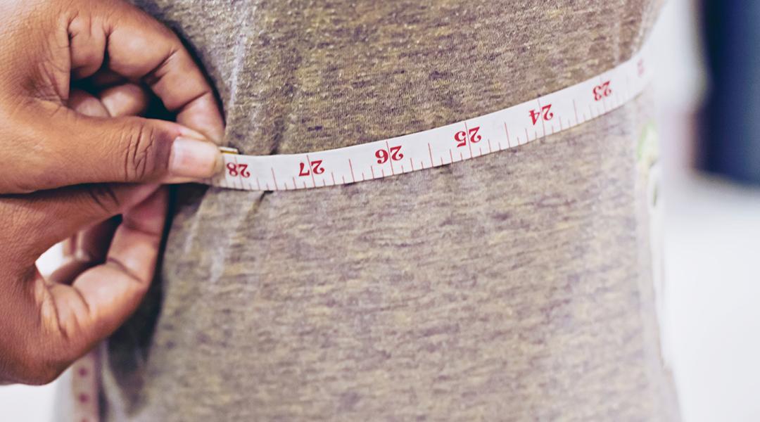 A tailor taking measurements of a client's torso with a tape measure.