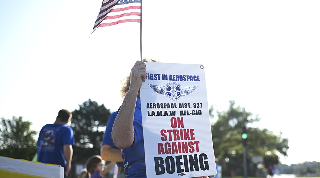 Boeing defense plant workers holding up "Strike Against Boeing" signs outside of a Boeing facility in Berkeley, Missouri.