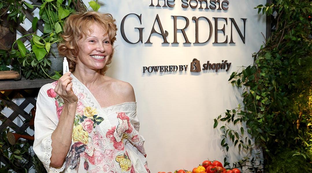 Pamela Anderson poses holding up a lip produce in front of "Sonsie Garden" with Shopify on October 24, 2025 in New York City.