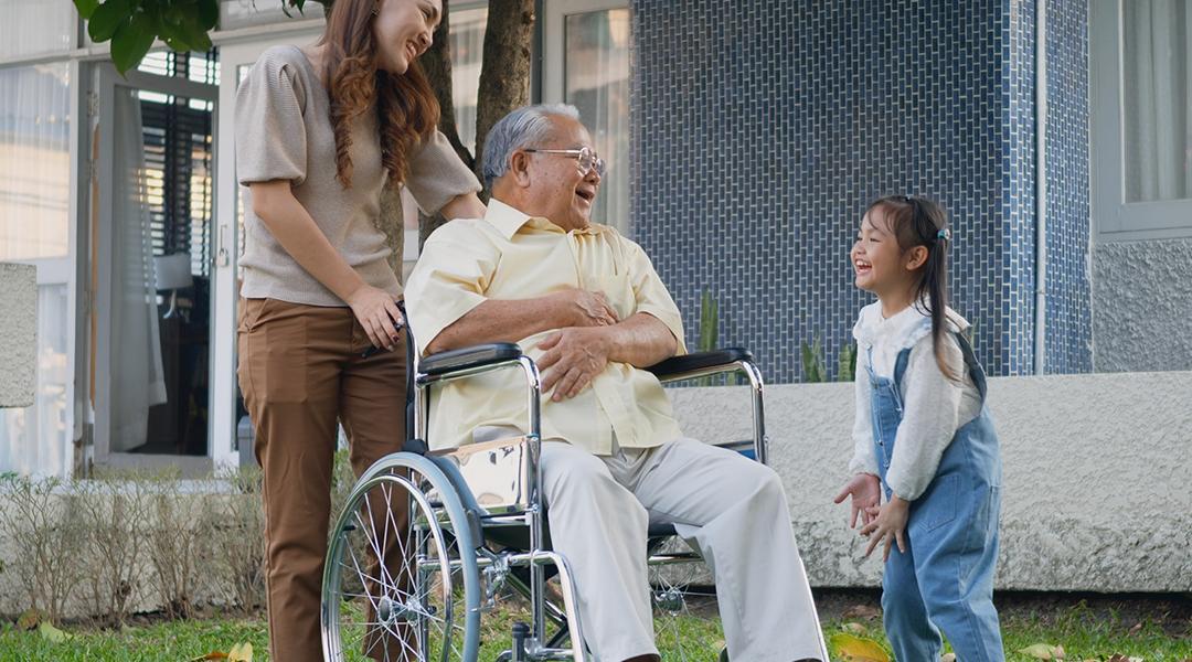 A disabled senior grandfather with his daughter and grandchild in a park.