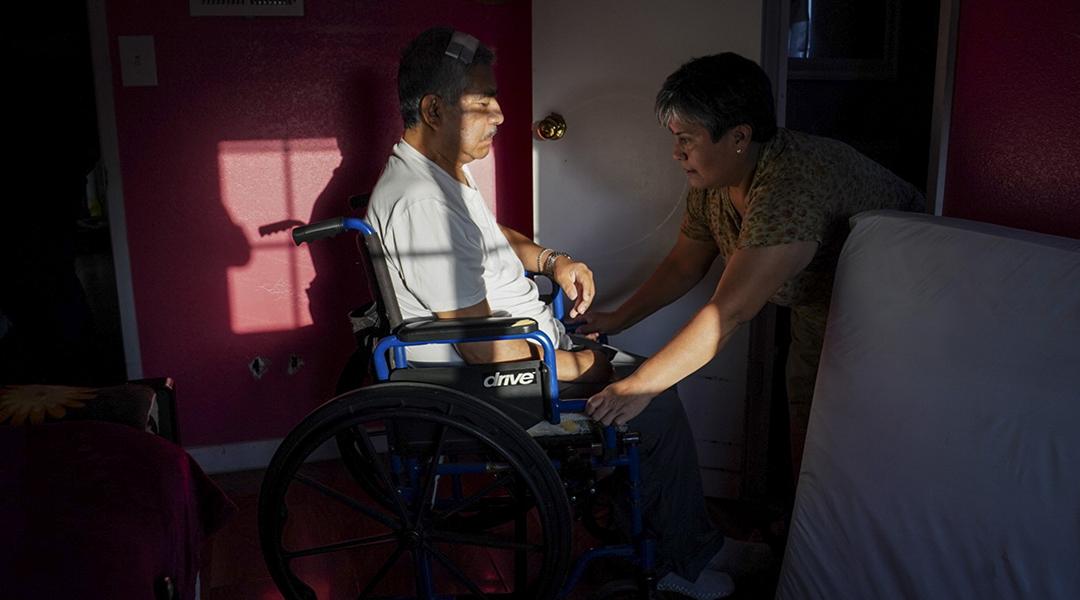 Maria Patricia Alcantara (R), wheels Jose Epifanio Sanchez Trujeque (L) to the bathroom at their home in Lebec, California.