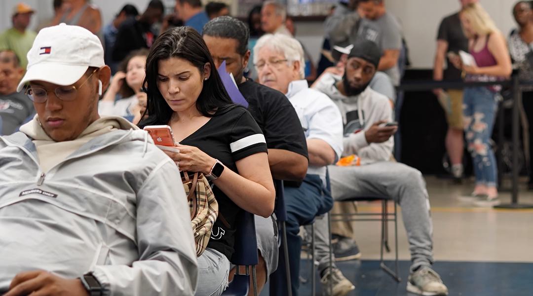 People seated for a queue where most are waiting by being on their phones.