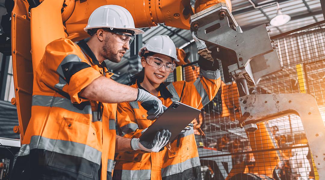 Two members of an engineering team looking at programming in a tablet inside their automated manufacturing factory.