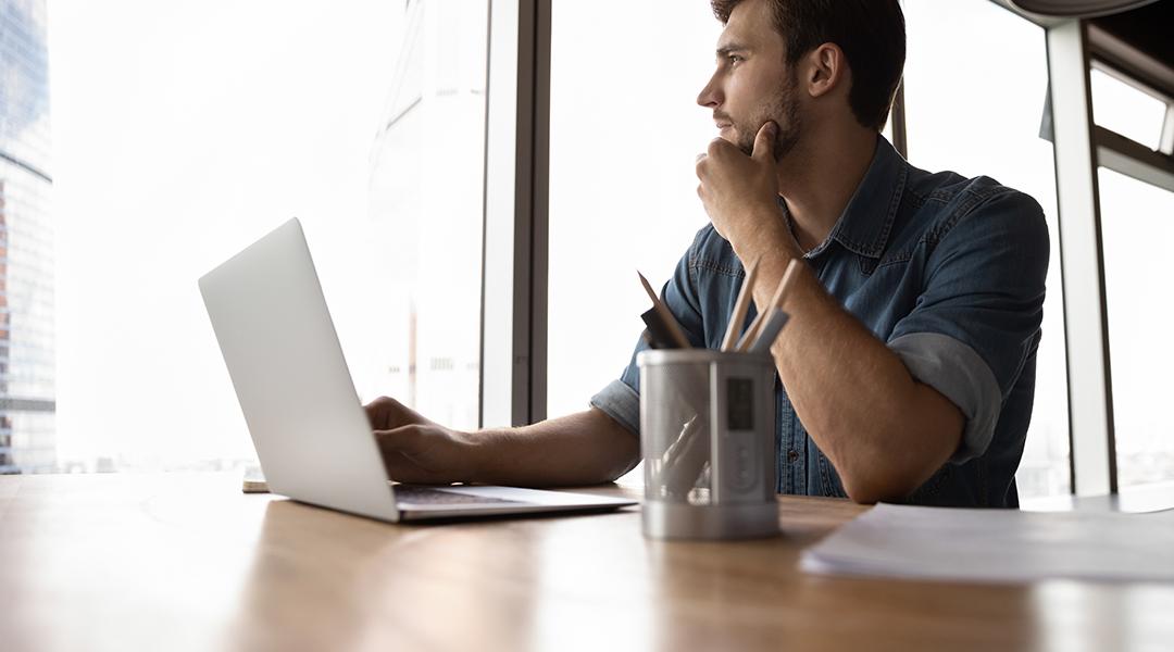 A male professional looking out the office window, pondering on work decisions.