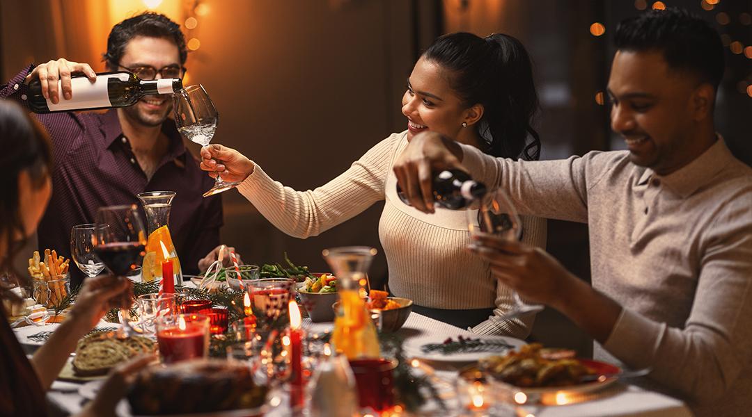 A group of happy friends pouring wine in their glasses during Christmas dinner.