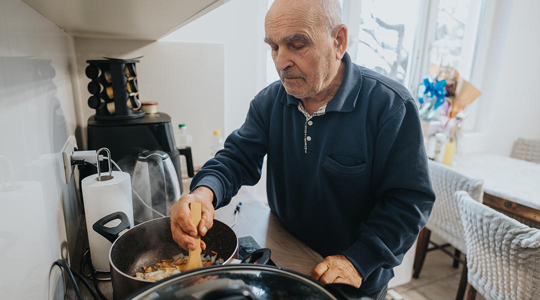 A senior man cooking a dish in his brightly-lit kitchen at home.