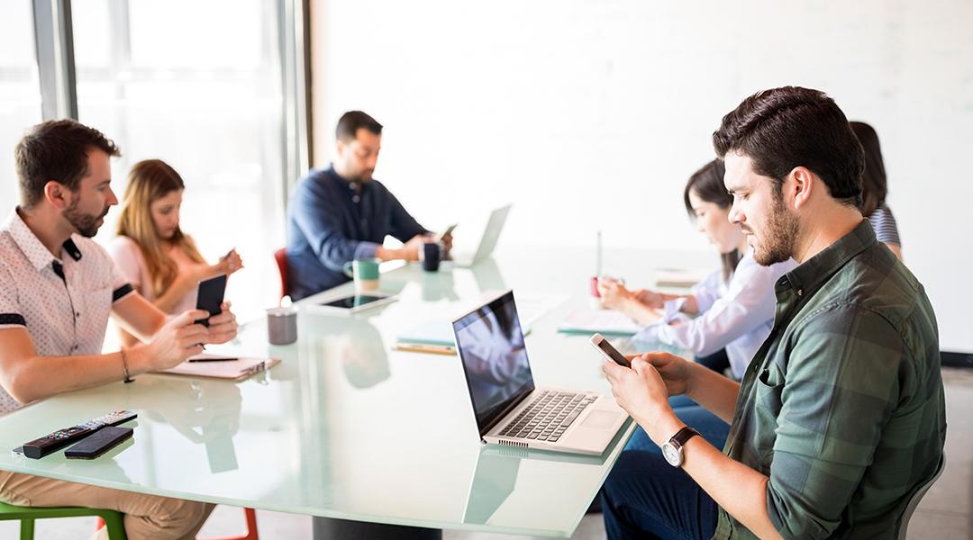 A business team in a meeting room but each member is using their phone.
