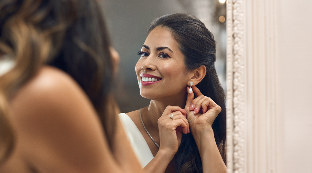 A woman looking at the mirror putting on her earrings.