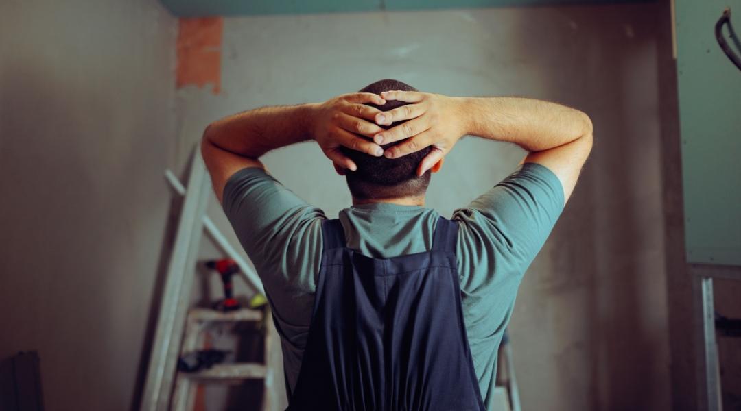 Back view of a construction worker with hands on head as he notices mistakes in a project.
