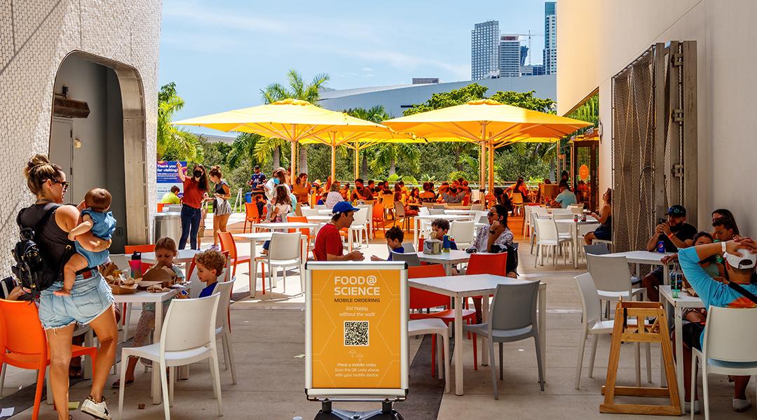 Outdoor dining areas at the Frost Museum in Florida where QR codes are seen for information and menu access.