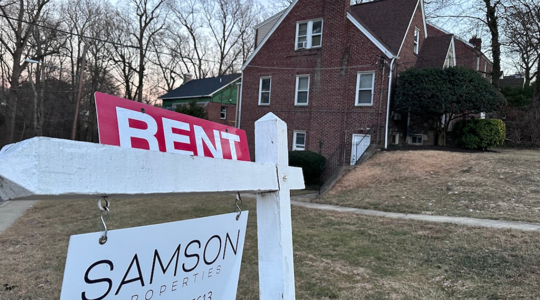 A sign in foreground lists a home for rent in Maryland with tall brick home in the background. Municipal rental registries are gaining attention as cities try to get a handle on who owns rental properties and where, both to better understand their housing landscape and to ensure rentals are safe for tenants. 